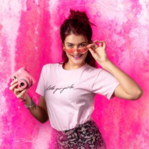 zelfverzekerde vrolijke jonge vrouw met zonnebril en roze camera tegen felroze achtergrond