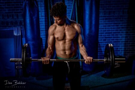 portretfotografie sterk beeld van jonge gespierde sporter met zware halter tegen blauwe muur bijzondere manier van fitness in het voormalig juvenaat zevenaar