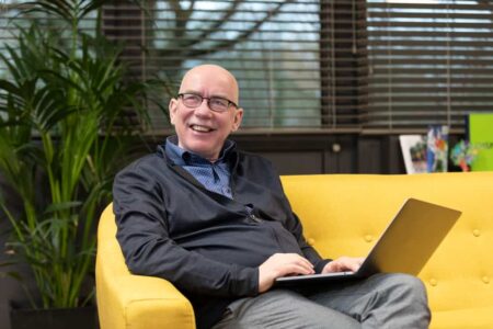foto van bedrijfseigenaar op gele bank met laptop